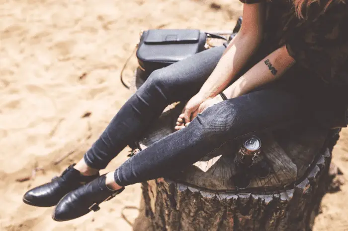 person wearing a blue denim jeans and black leather shoes sitting on a trunk