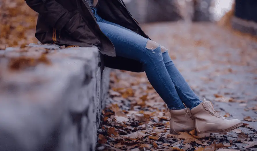 girl wearing ripped jeans sitting on the park wall