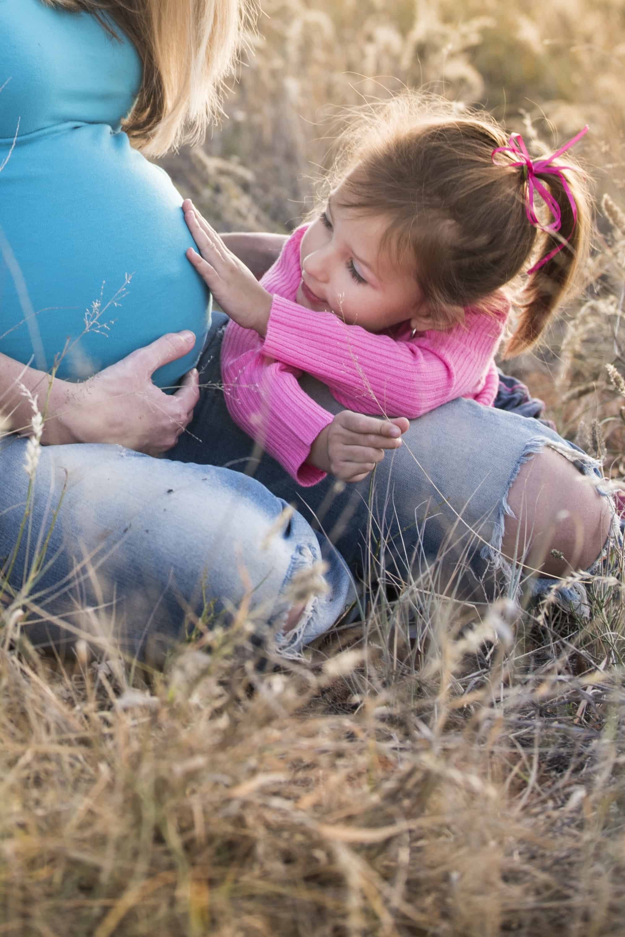 Little girl is touching the tummy of her pregnant mother while the mother is wearing the best maternity jeans